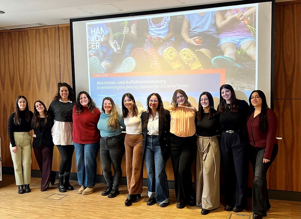 Gruppe von elf Frauen steht lächelnd vor einer Präsentationsleinwand mit deutschem Text in einem Konferenzraum.