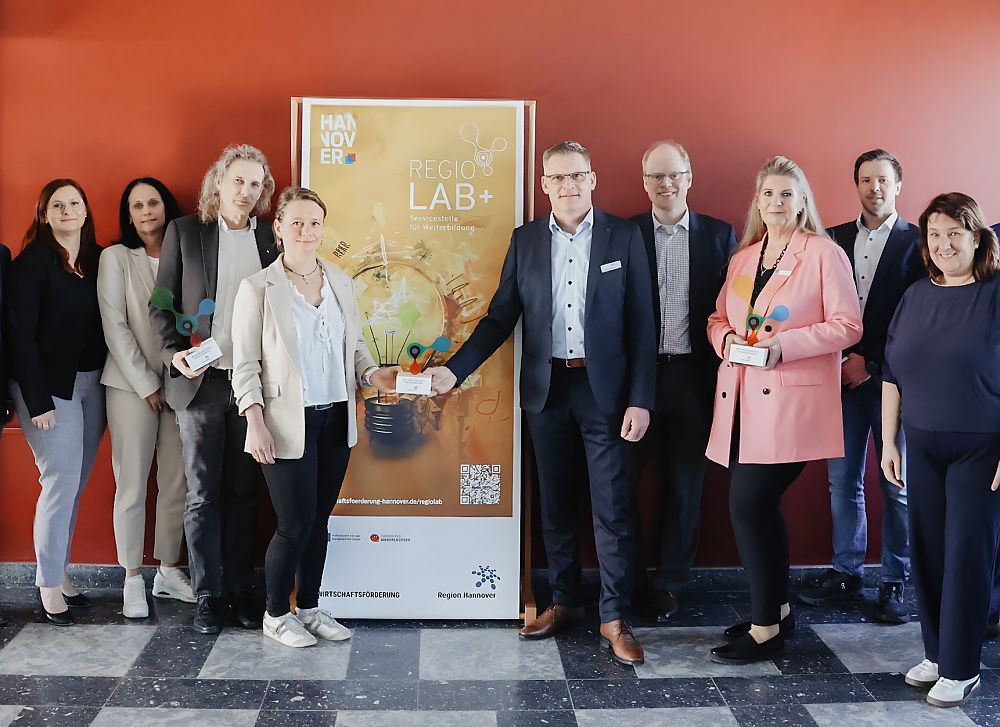 Gruppe von ca. 11 Personen steht vor einem Banner mit Aufschrift „REGIO LAB+" in einem Gebäude.